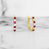 Gold hoop earrings with ruby and diamonds on a light gray background